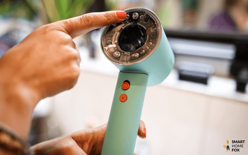 Der Bedienknopf für den Kopfhautschutzmodus des Dyson Supersonic Nural wird mit einem Finger anvisiert.